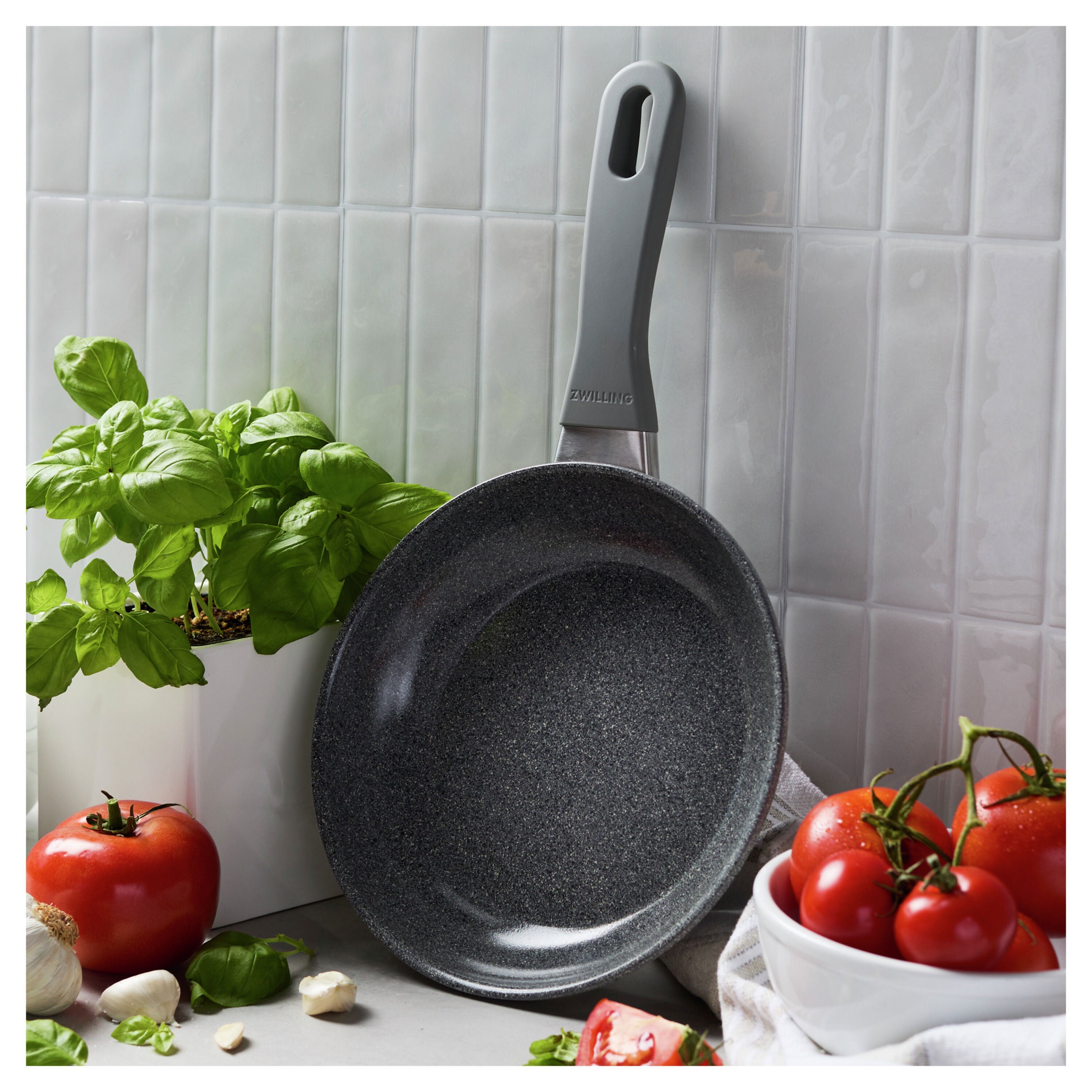 Gray frying pan on a kitchen counter with tomatoes and basil