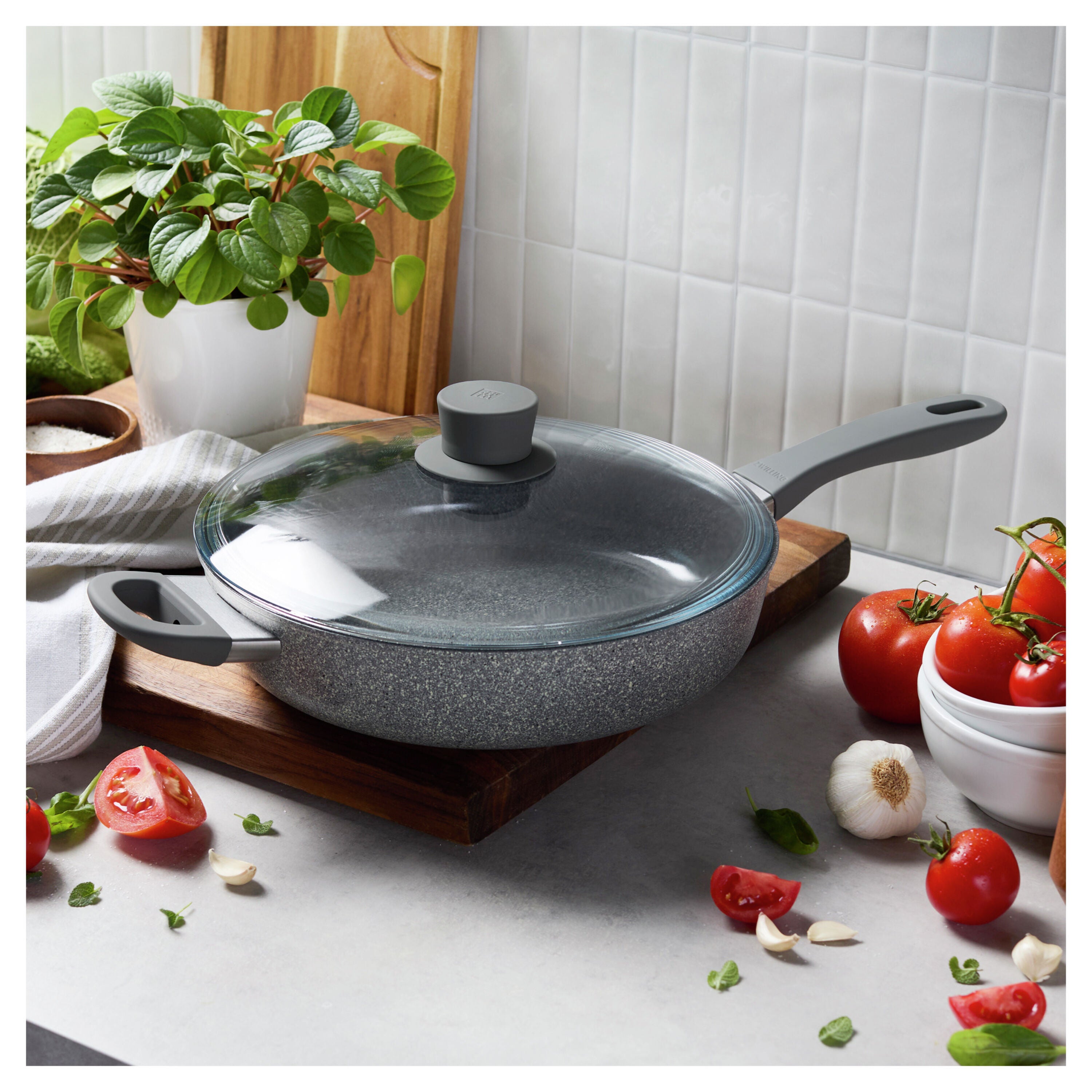 Gray speckled cookware set on a kitchen counter with tomatoes and herbs.