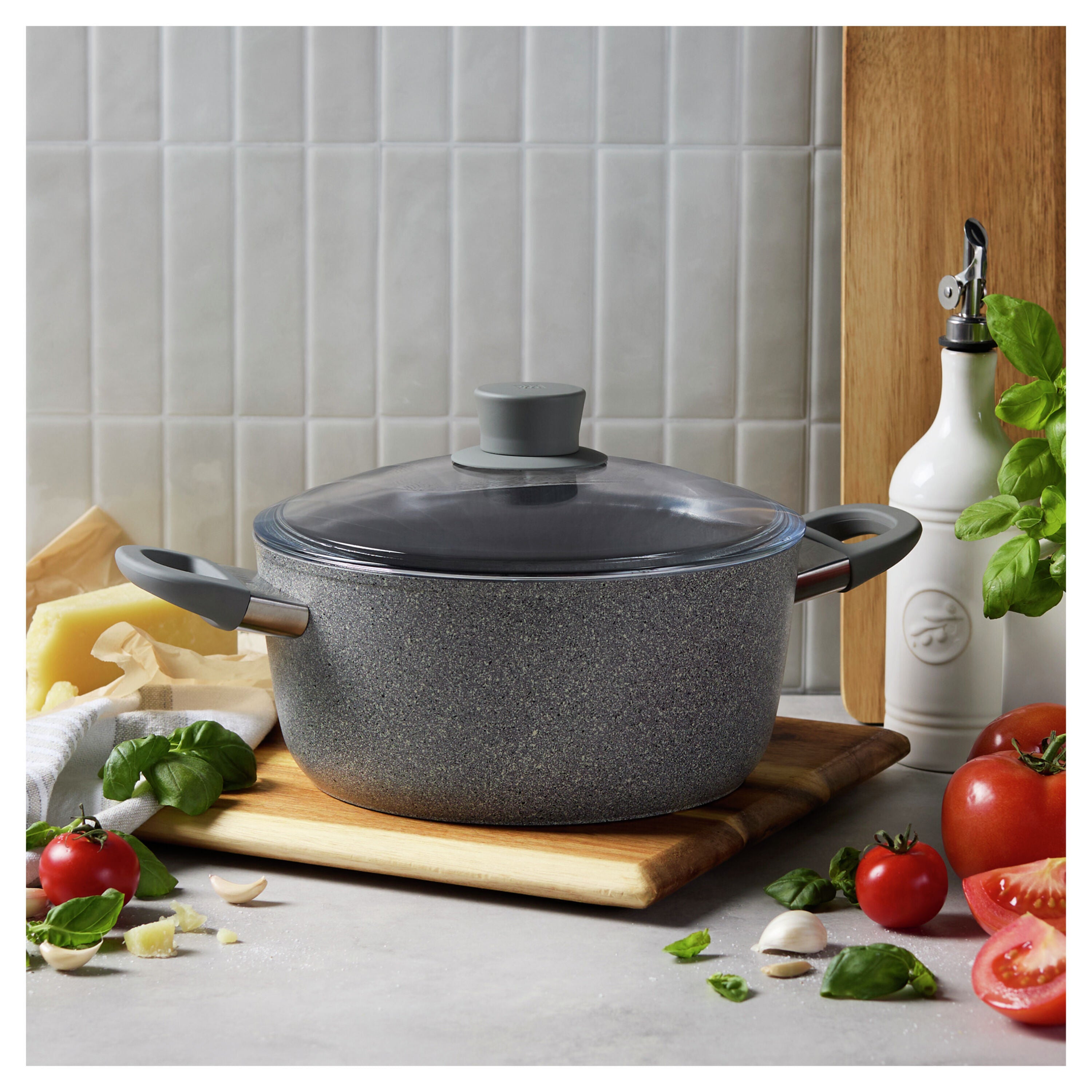Gray speckled cookware pot with lid on a kitchen counter with tomatoes and herbs