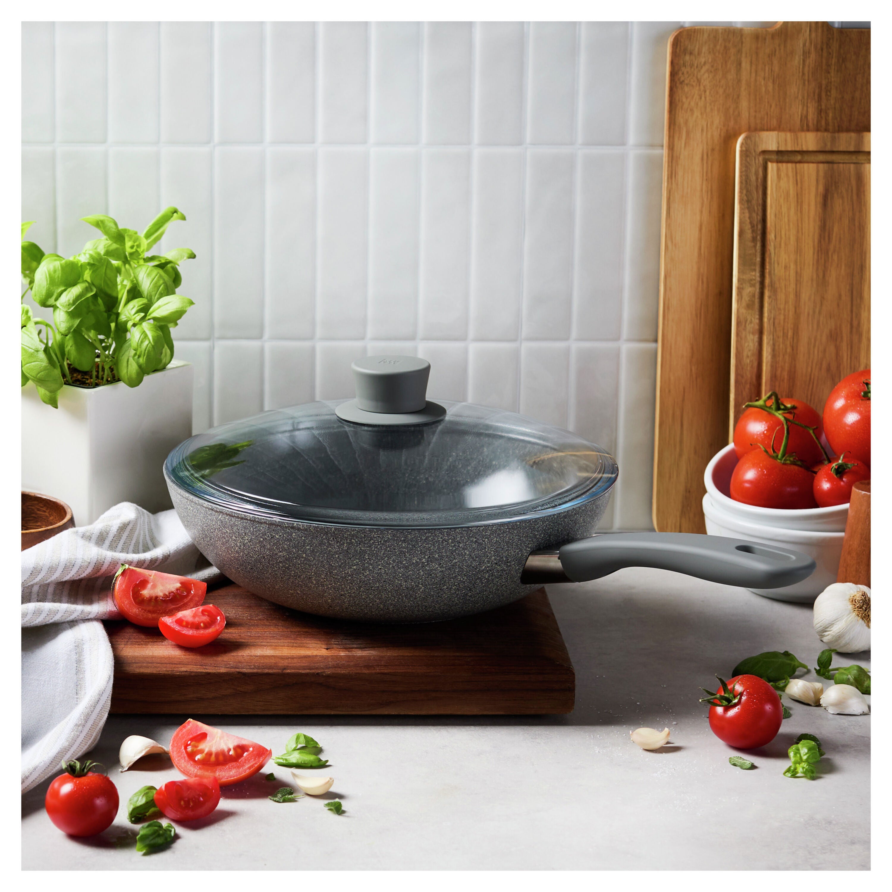 Gray frying pan with lid on a kitchen counter with tomatoes and basil