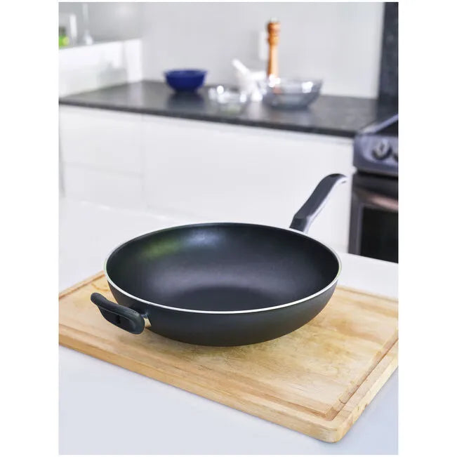 Black frying pan on a wooden cutting board in a kitchen setting