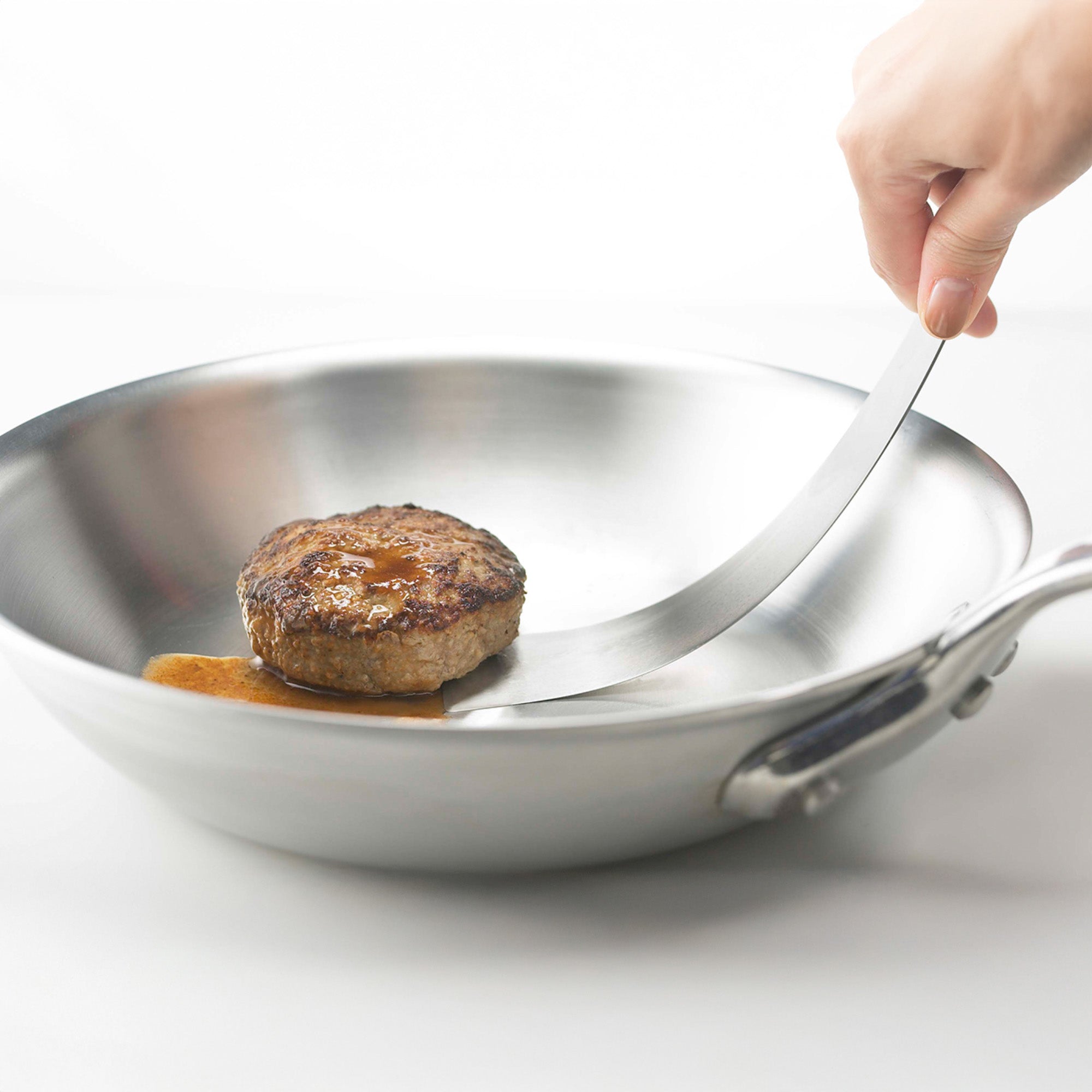 Stainless steel frying pan with a cooked steak on a white background