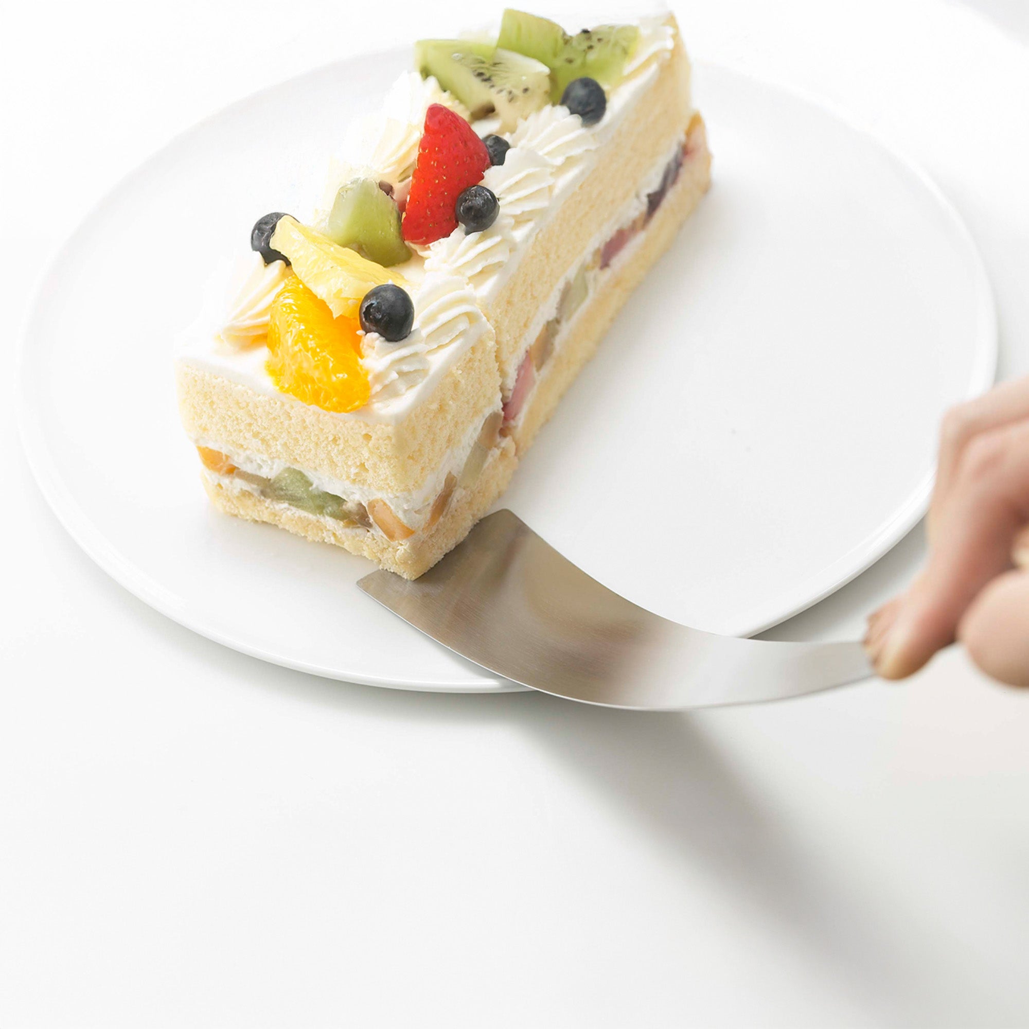 Slice of fruit cake on a white plate with a hand holding a spatula