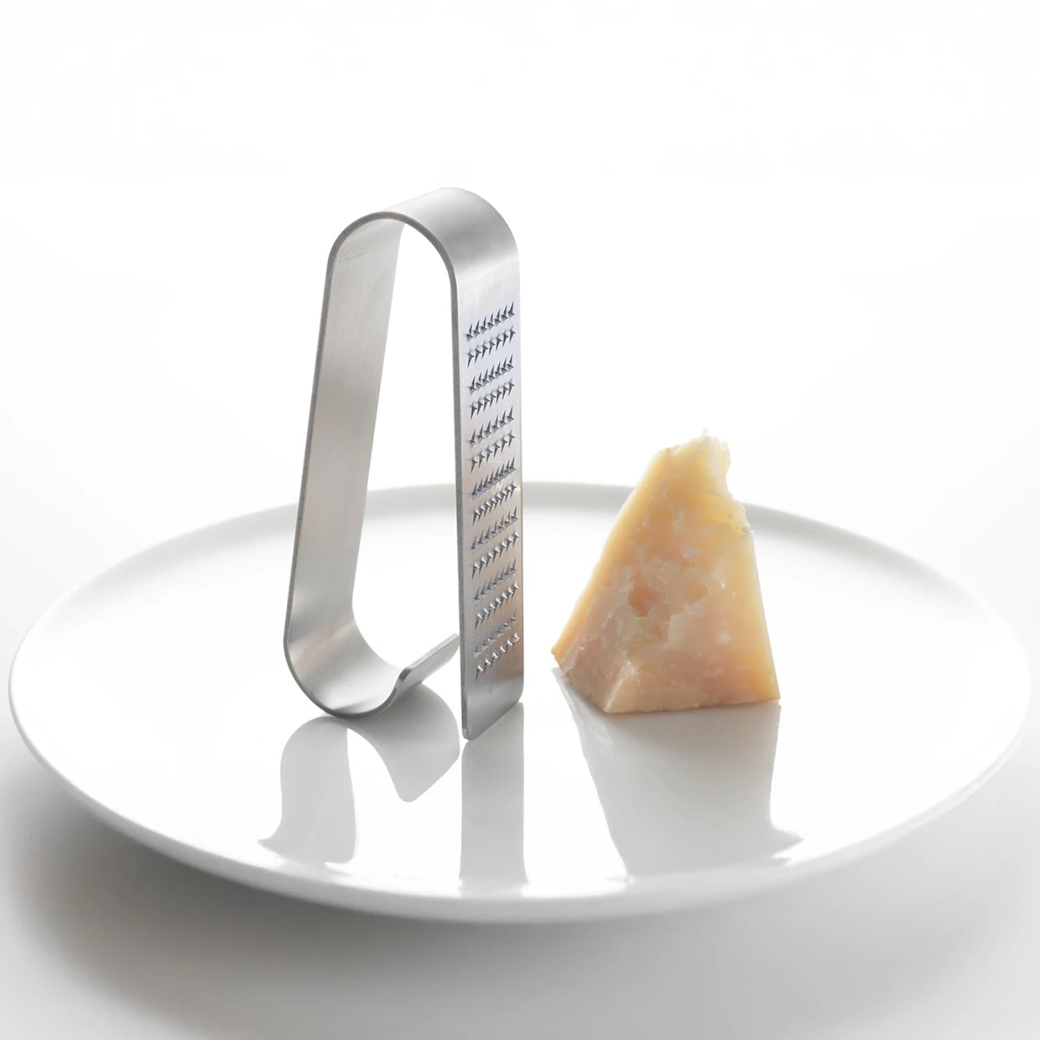 Metal cheese grater next to a wedge of Parmesan cheese on a white plate
