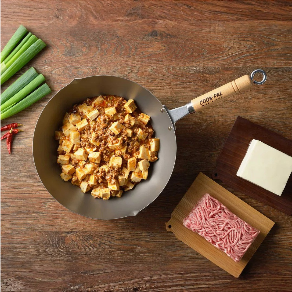 Wok with stir-fried dish on a wooden table with ingredients and a brand name visible