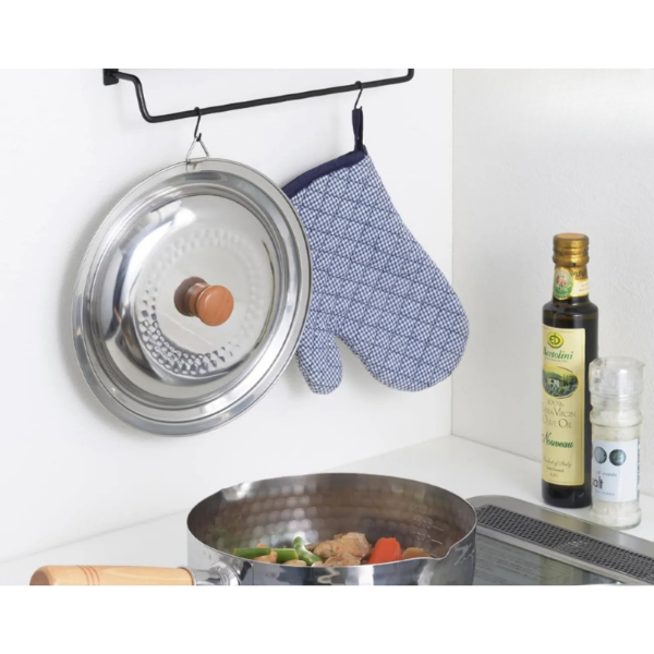Stainless steel pot with lid, pan on stove, and kitchen items on a white background