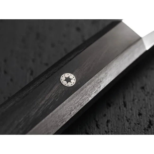Close-up of a knife with a brand embedded on a textured black wood 
background