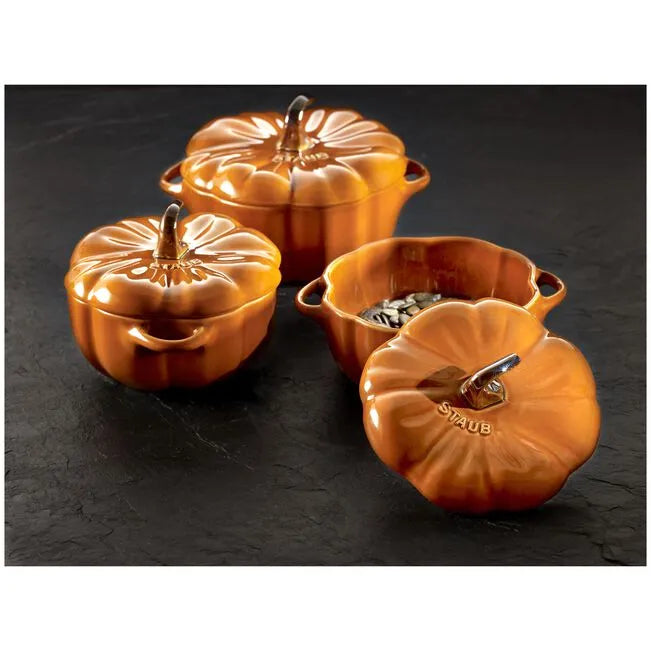 Set of four orange pumpkin-shaped Staub cookware on a dark surface