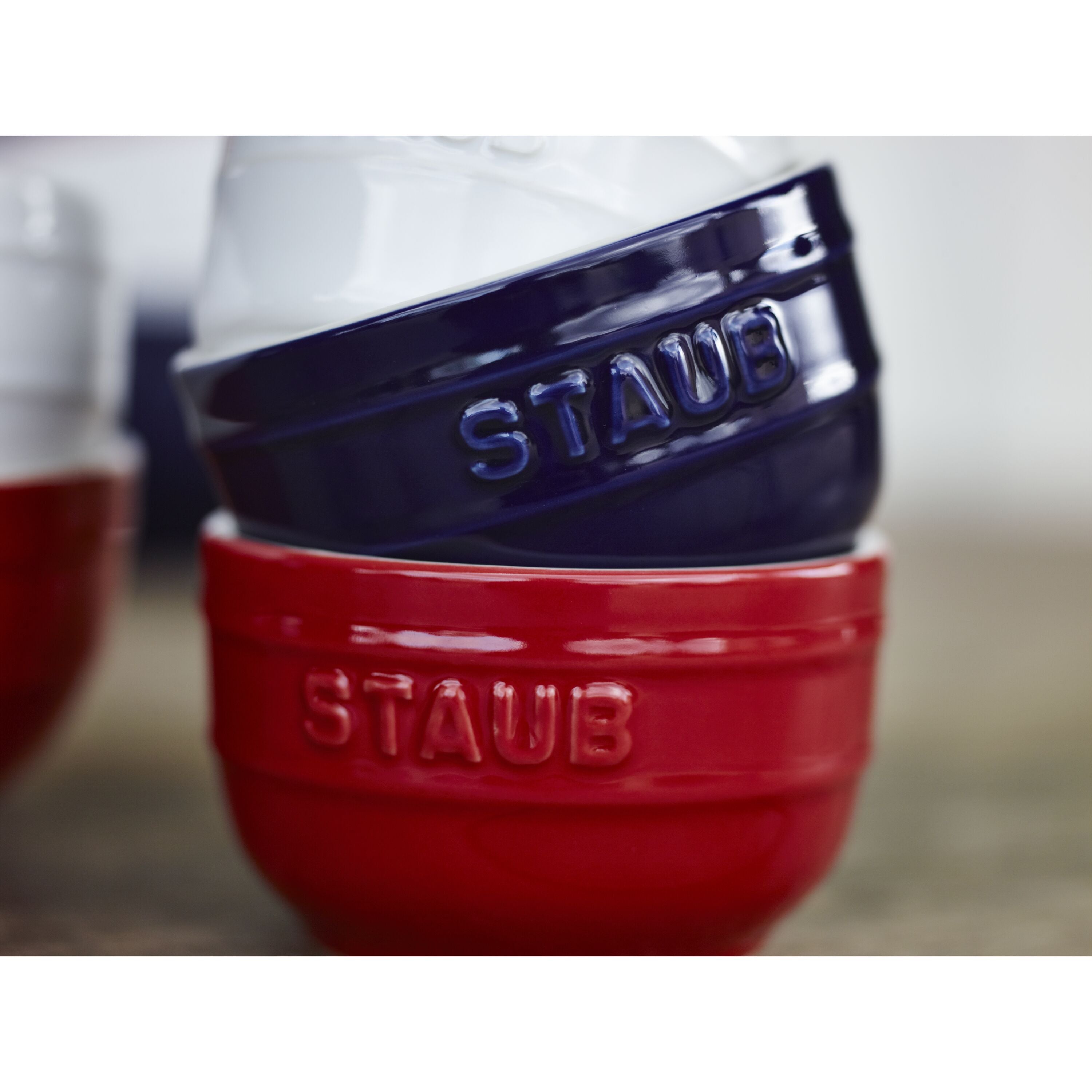 Red and blue Staub cookware pieces on a neutral background
