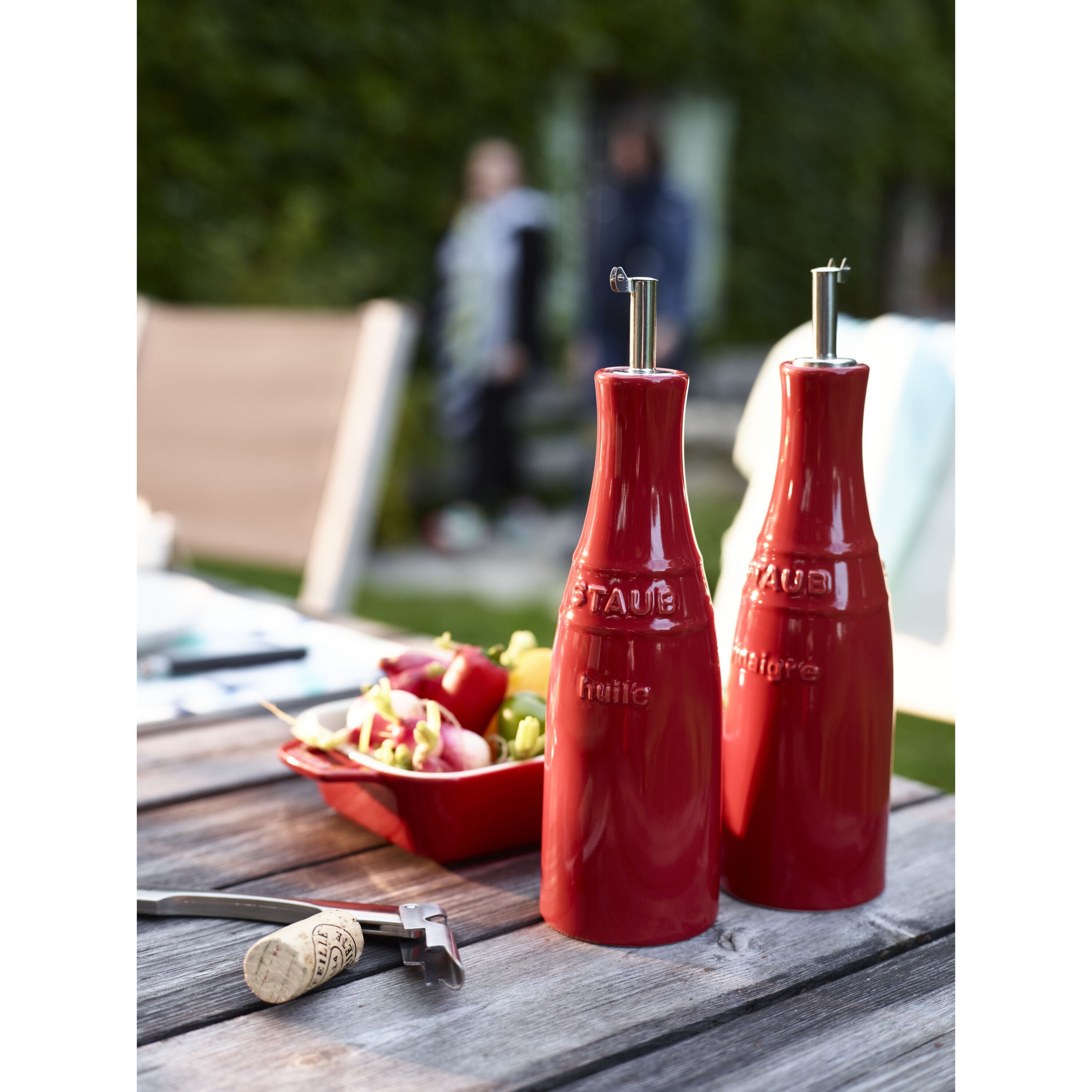 STAUB Ceramique Ceramic Oil And Vinegar Set on a table with salad, showcasing red ceramic bottles outdoors.