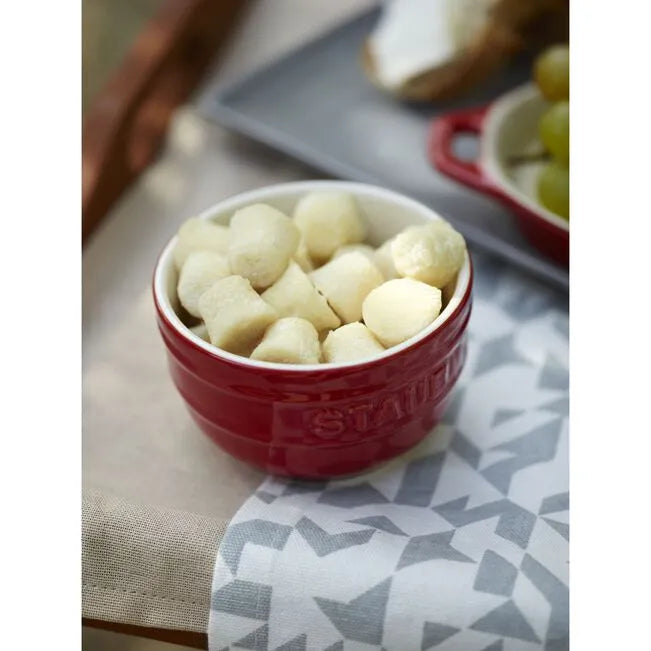 Red Staub bowl filled with white spherical objects on a patterned surface.