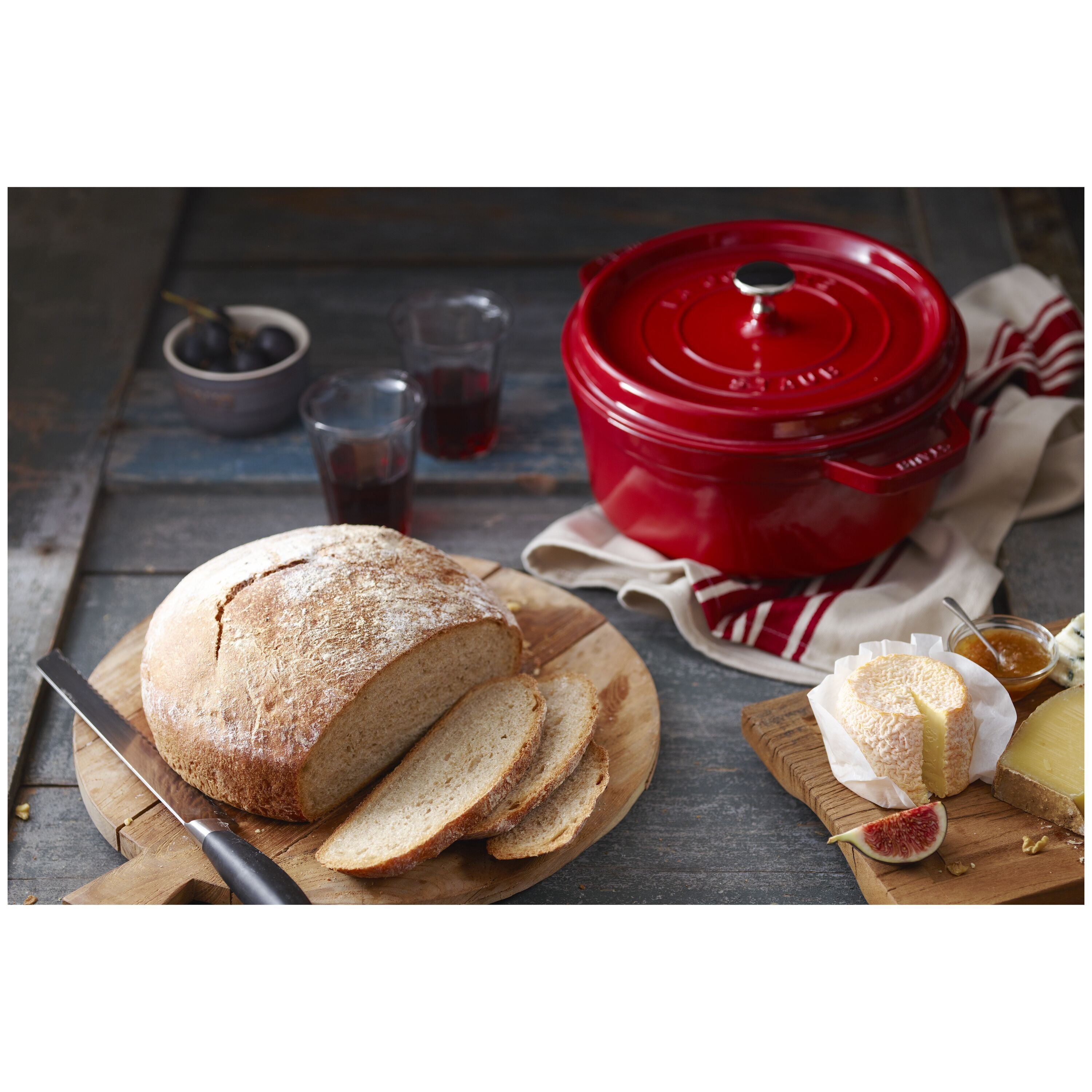 Red Staub cocotte with bread and cheese on a wooden table