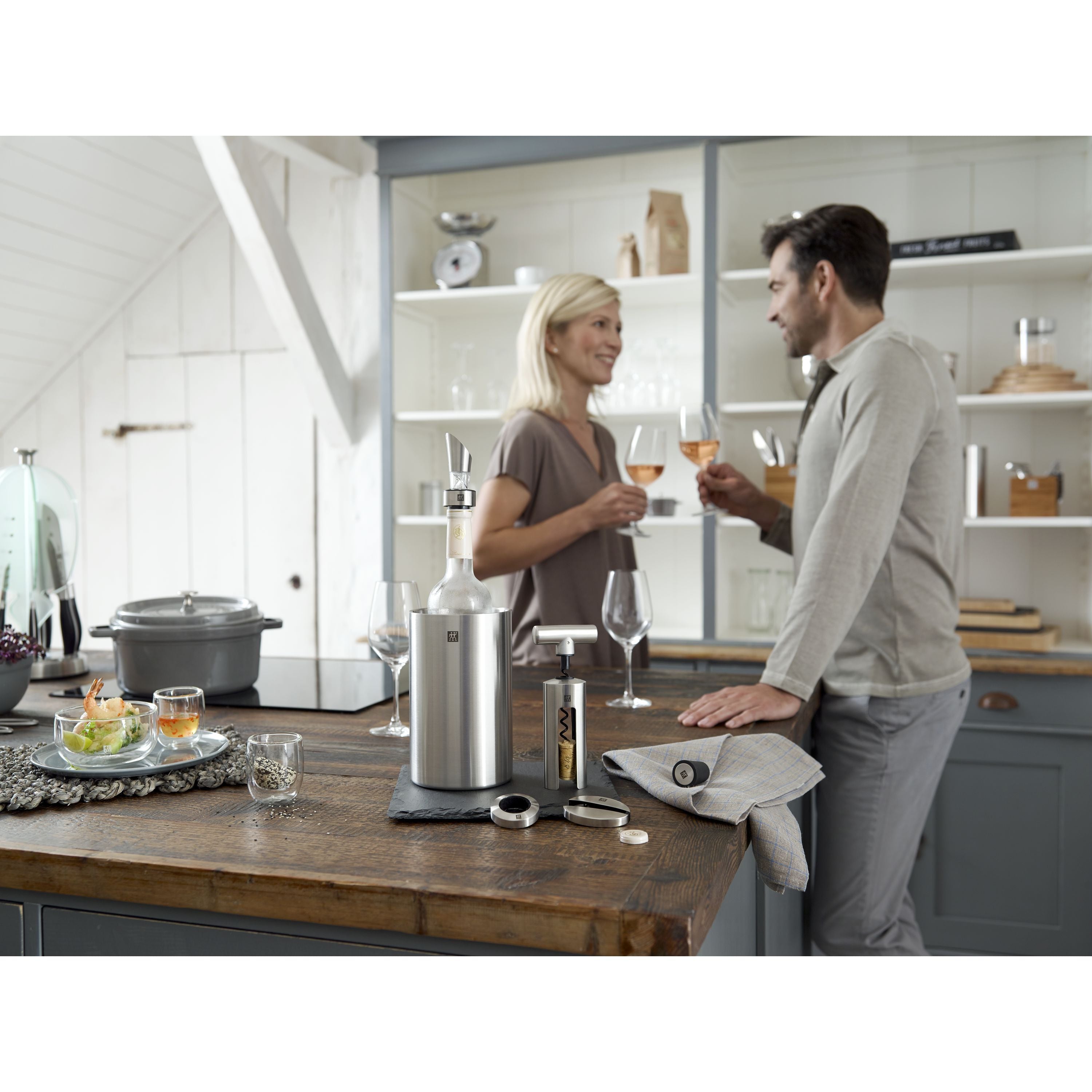 Man and woman standing in a kitchen with wine glasses, discussing something.