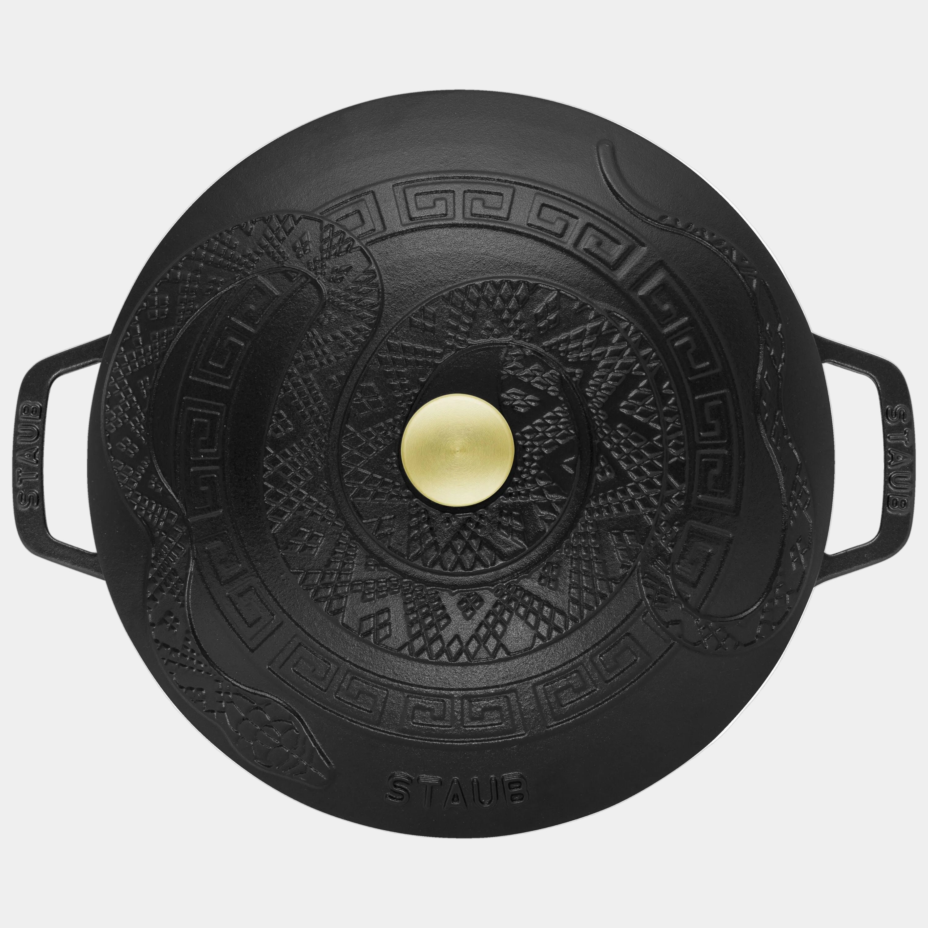Black cast iron lid with decorative patterns and a gold knob on a white background