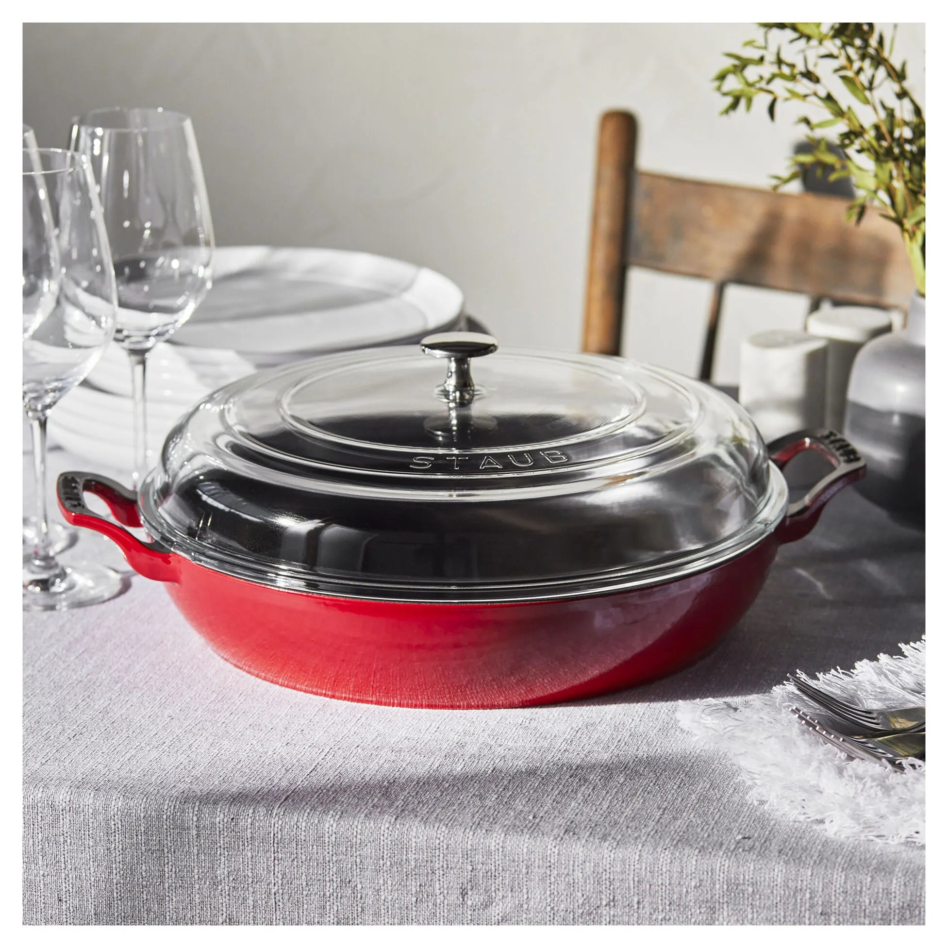 Red Staub casserole dish with clear lid on a table setting