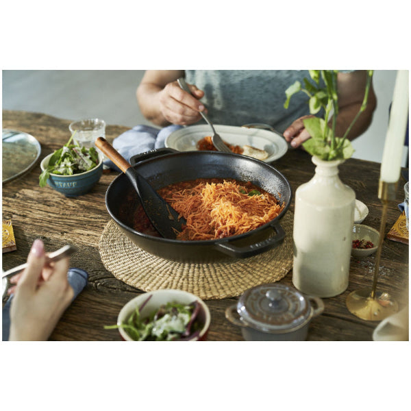 STAUB Specialities Cast Iron Wok People eating at a table with a pan of food on a wooden table.