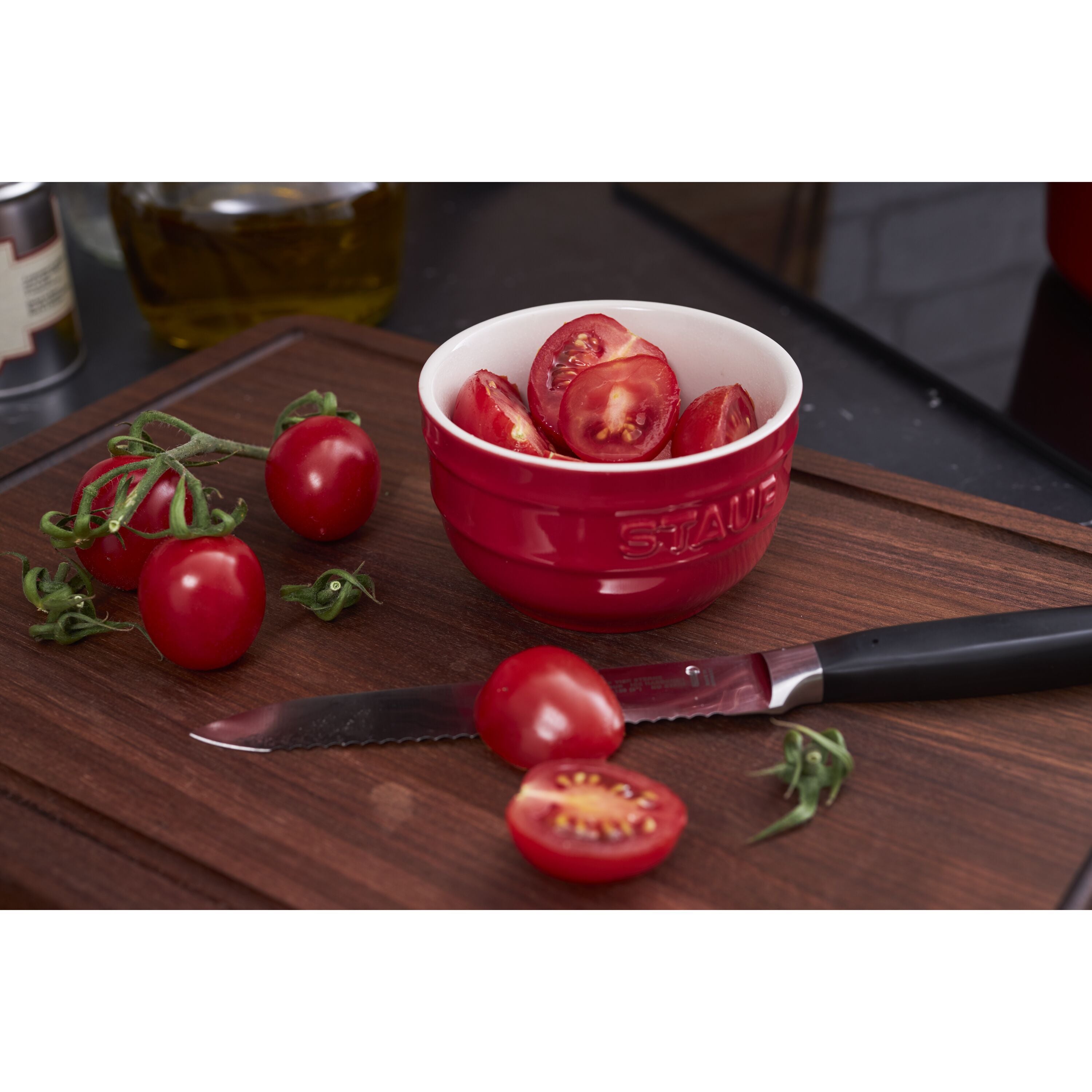 Red bowl with sliced tomatoes on a wooden cutting board with a knife.