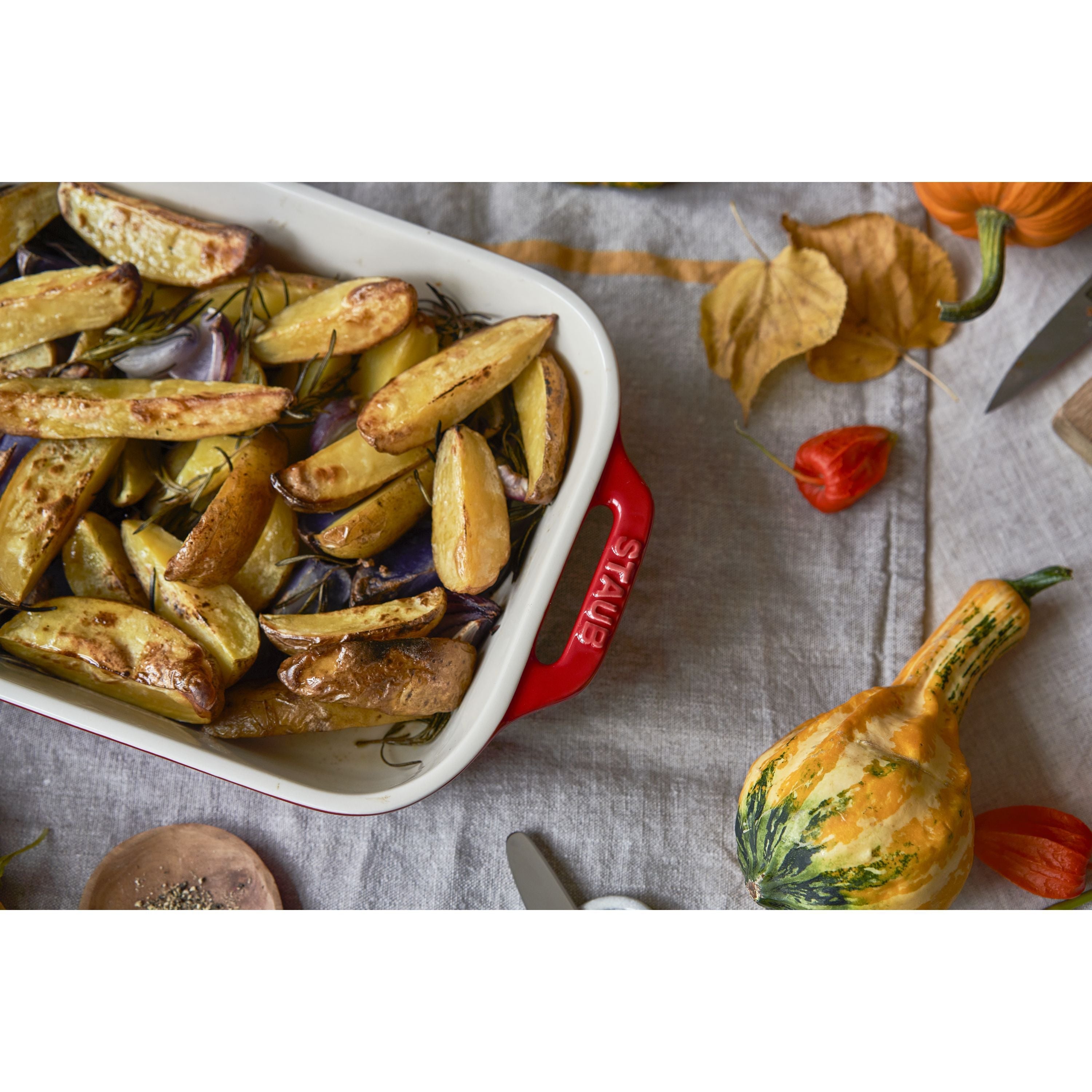 Roasted vegetables in a Staub dish on a rustic tablecloth with autumn decorations.