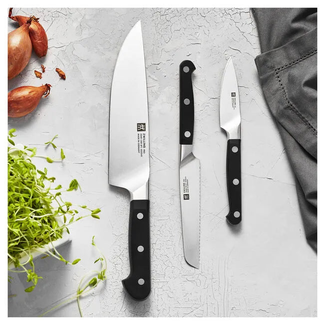 Set of knives with black handles on a light gray surface with vegetables.