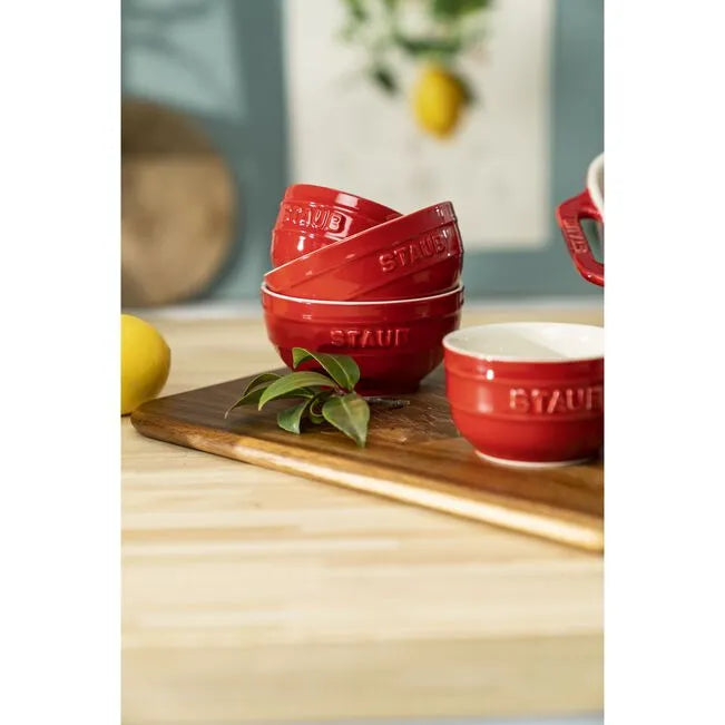 Red Staub ceramic bowls on a wooden surface with lemons and leaves.