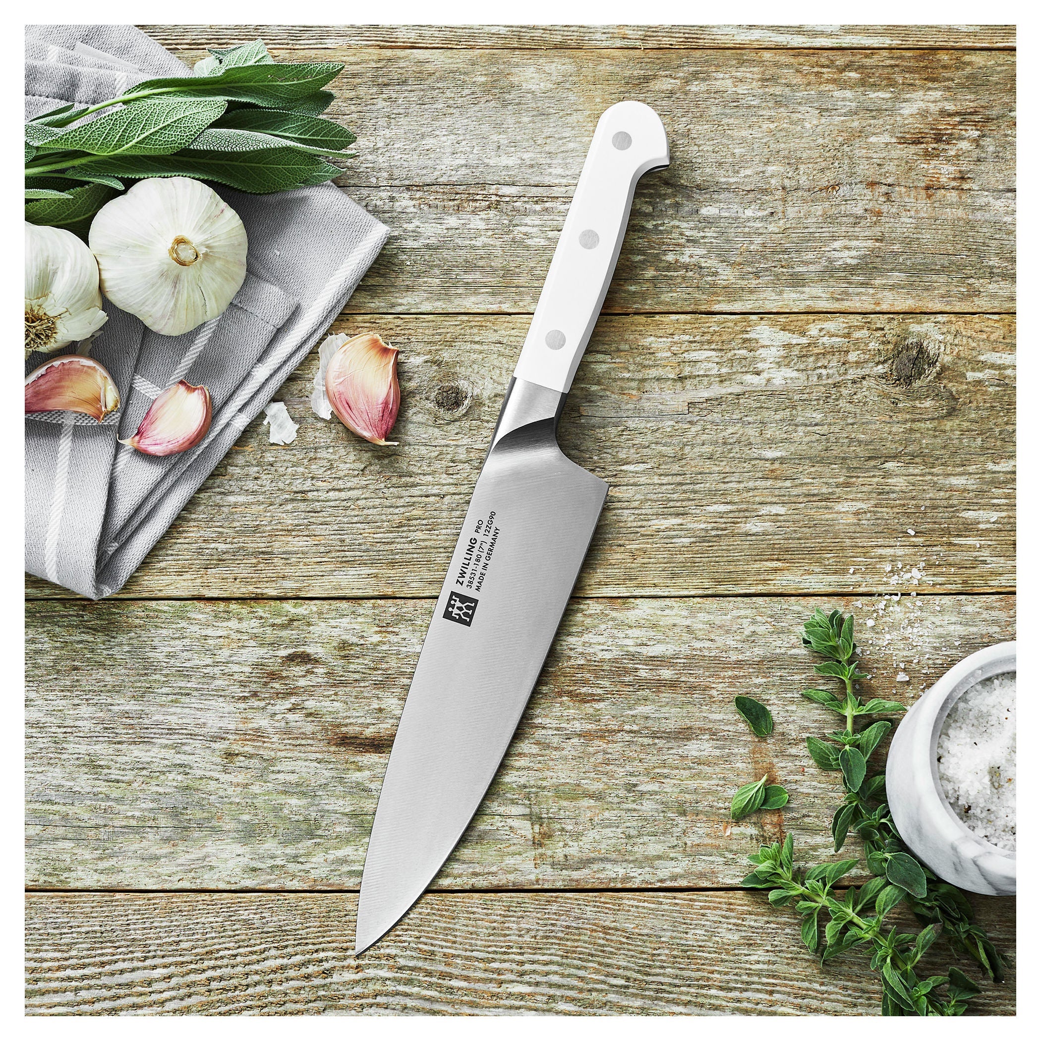 ZWILLING Pro le blanc 7 inch Chef's Knife, on a wooden surface with garlic and herbs