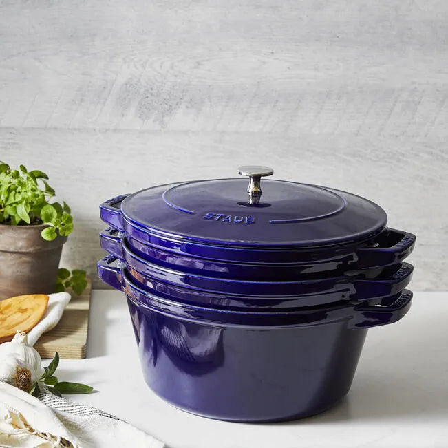 Set of blue Staub cookware on a light surface with a neutral background