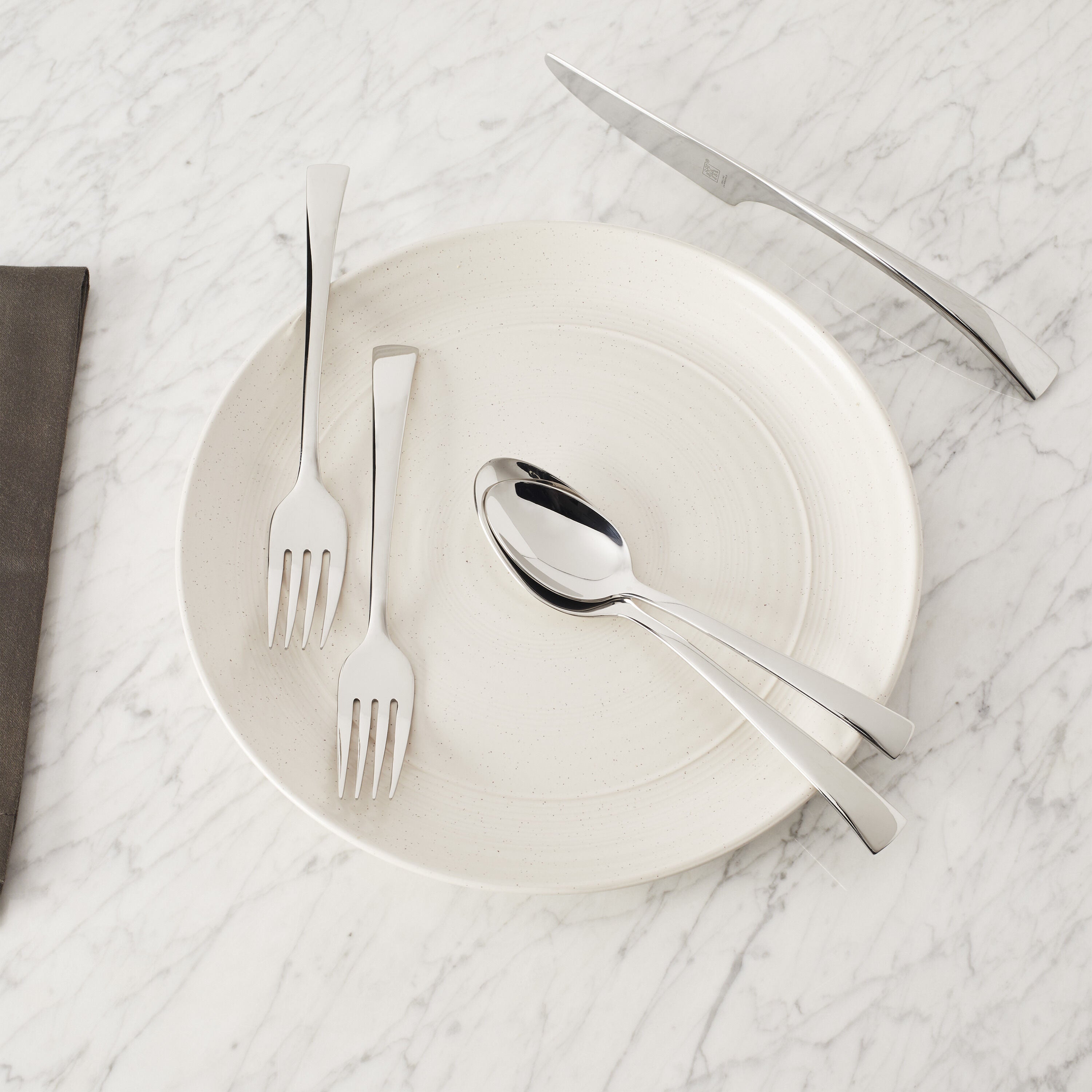 ZWILLING Bellasera 45 Pcs Flatware Set arranged on a plate, showcasing elegant polished 18/10 stainless steel design on marble table.