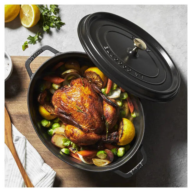 Roasted chicken with vegetables in a black cast iron dish on a wooden board.