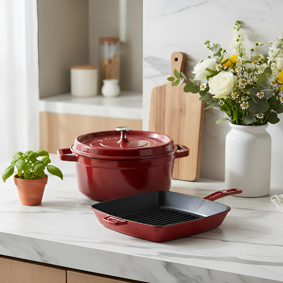 Red cookware set on a kitchen counter with flowers and a cutting board in the background.