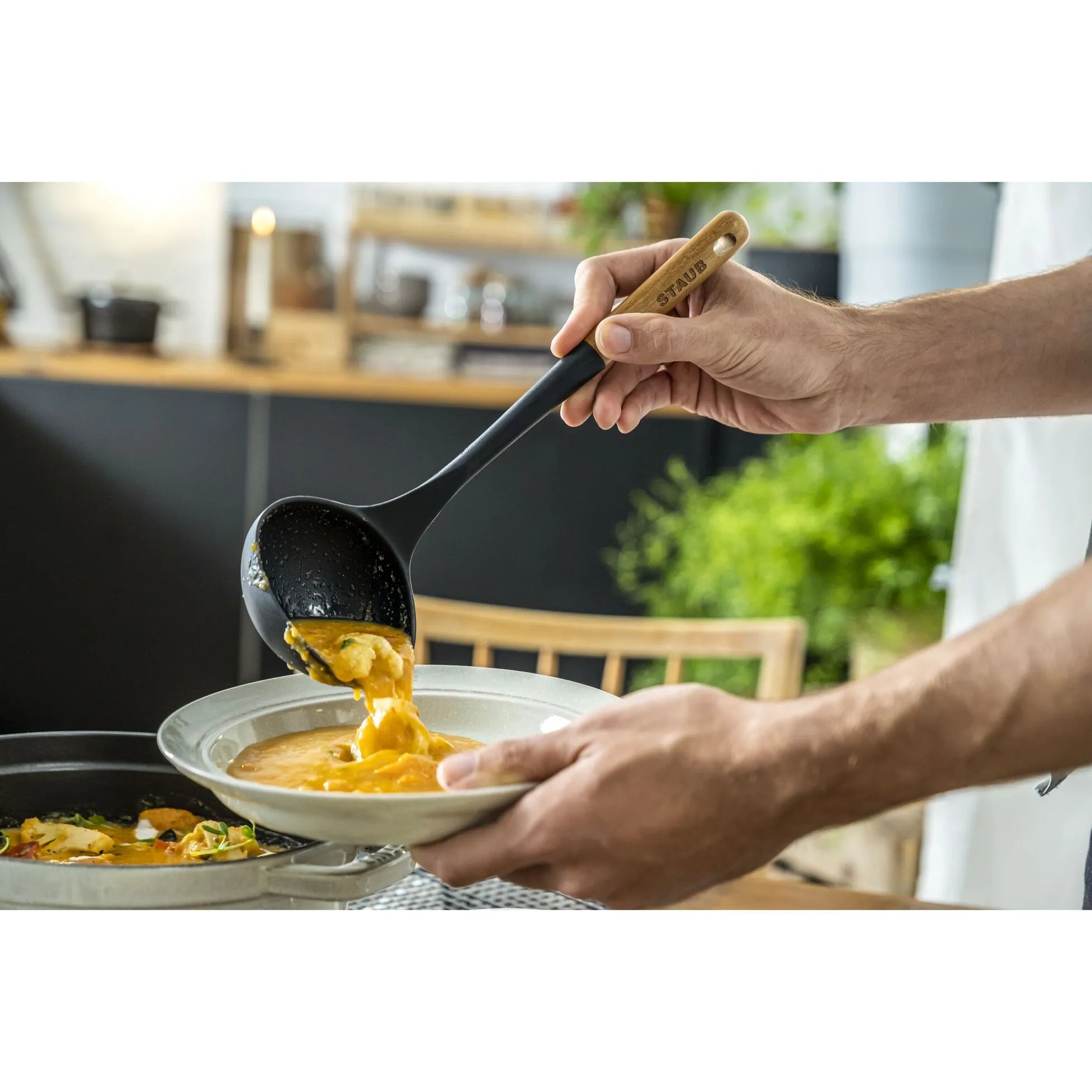 Person serving food from a pan into a bowl using a ladle.
