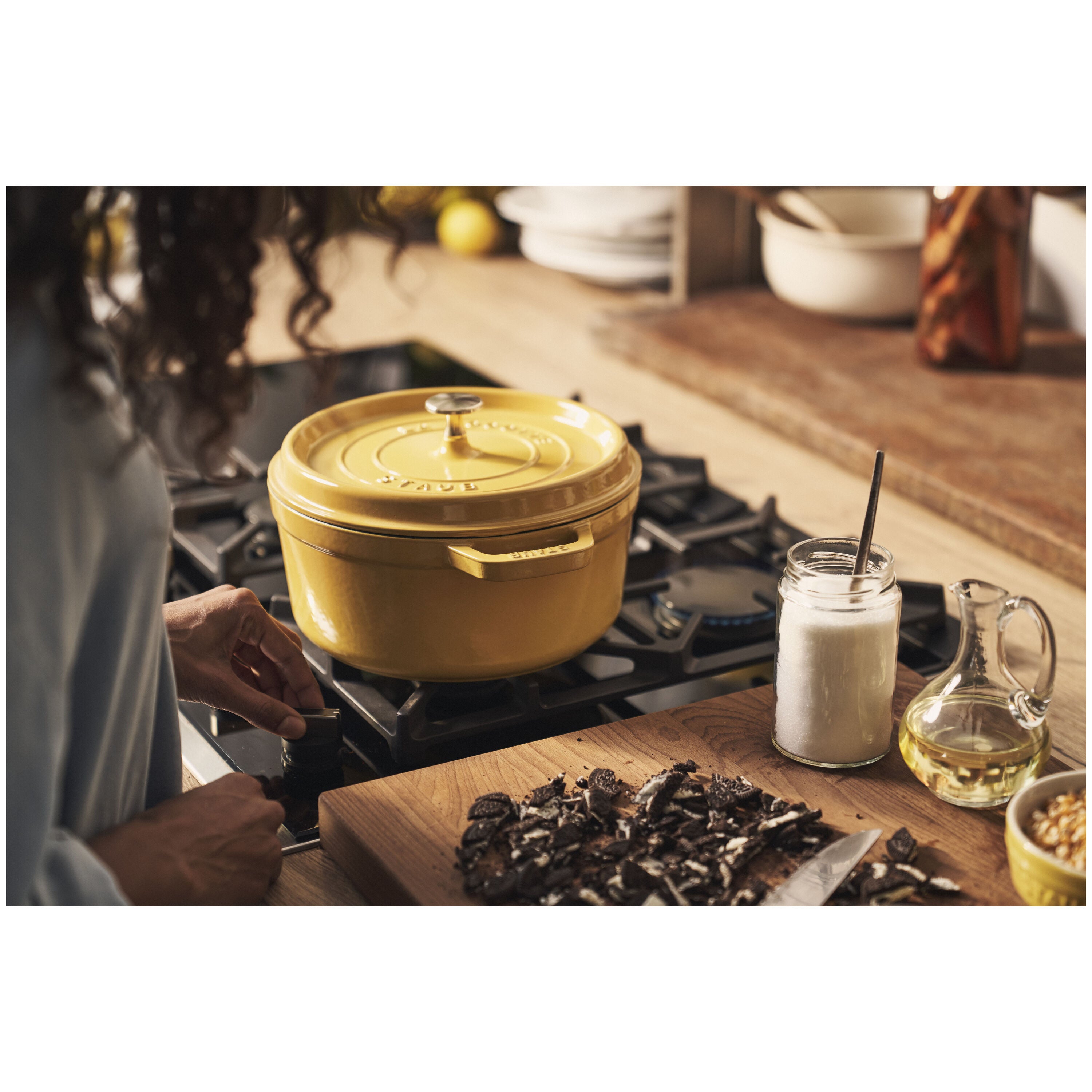 Yellow cast iron pot on a stove with a person cooking in the background