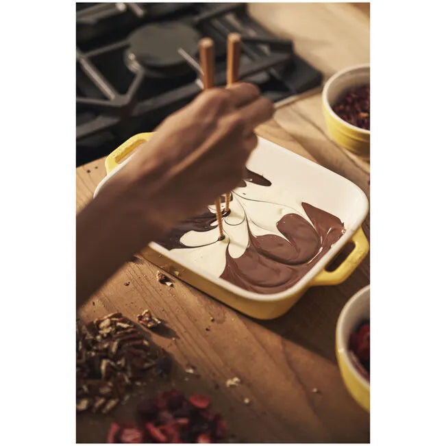 Person decorating a dessert with chocolate on a wooden table.