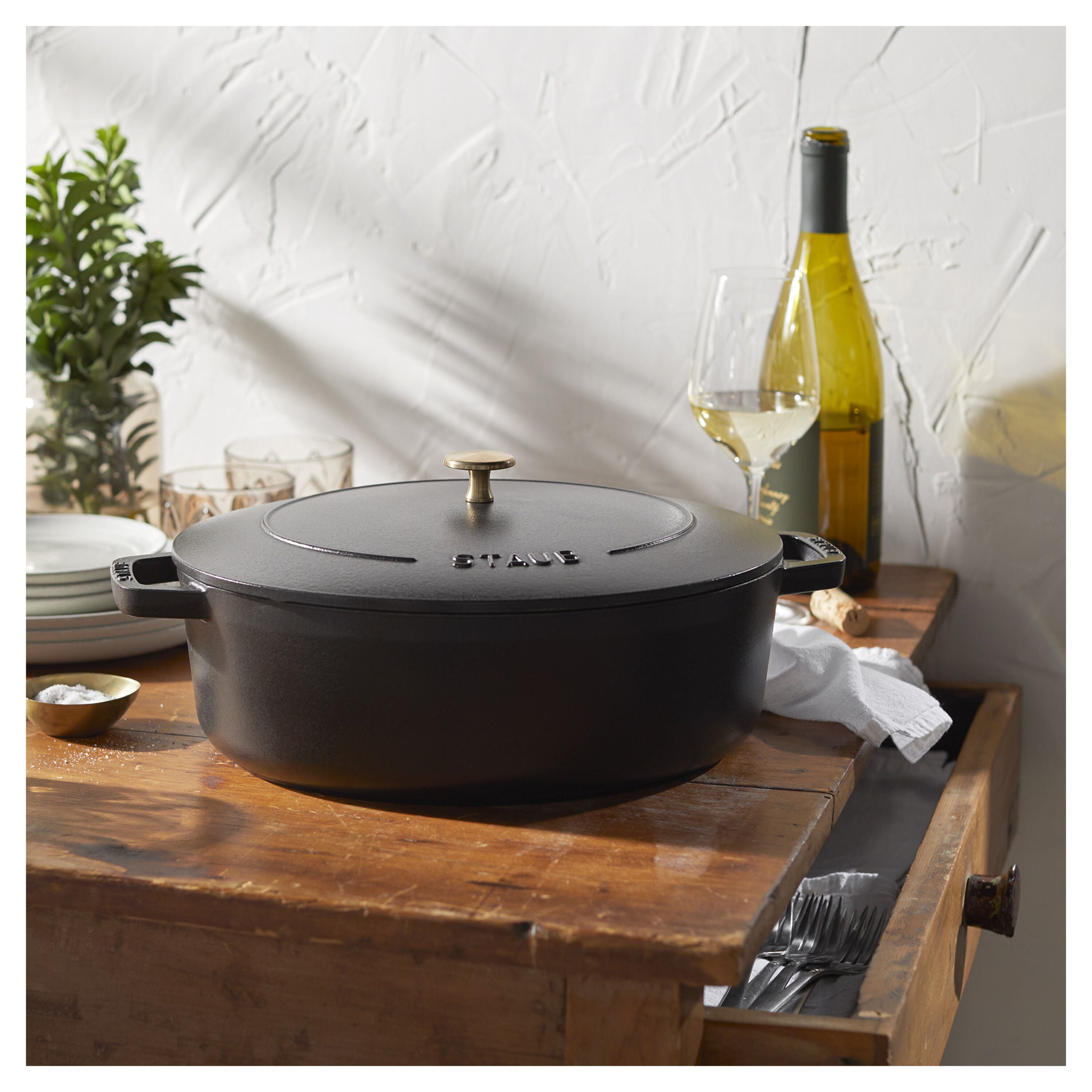 Black cast iron cookware on a wooden surface with a bottle of wine and glasses in the background.