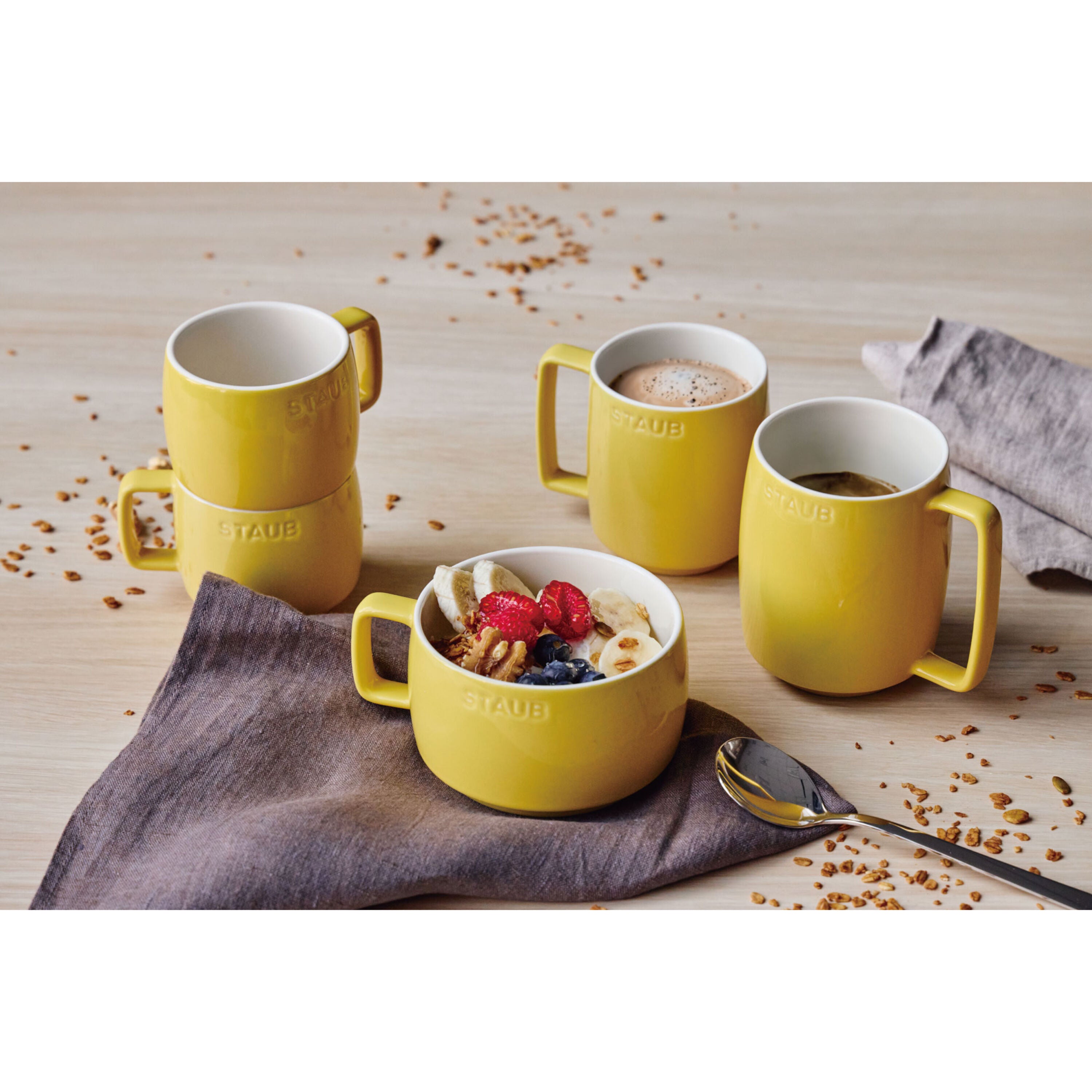 Yellow mugs on a wooden surface with cereal and berries.
