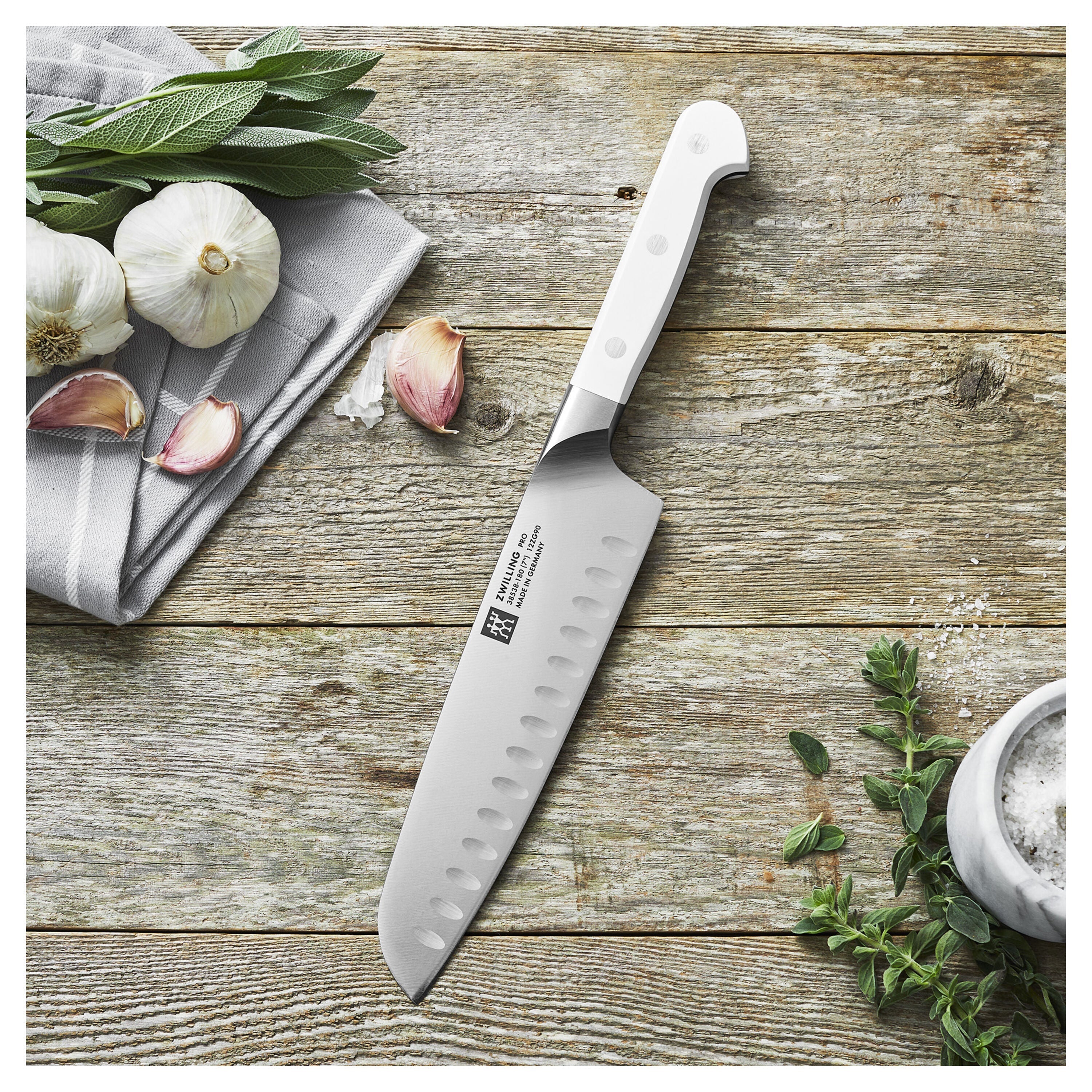 Chef's knife on a wooden surface with garlic and herbs