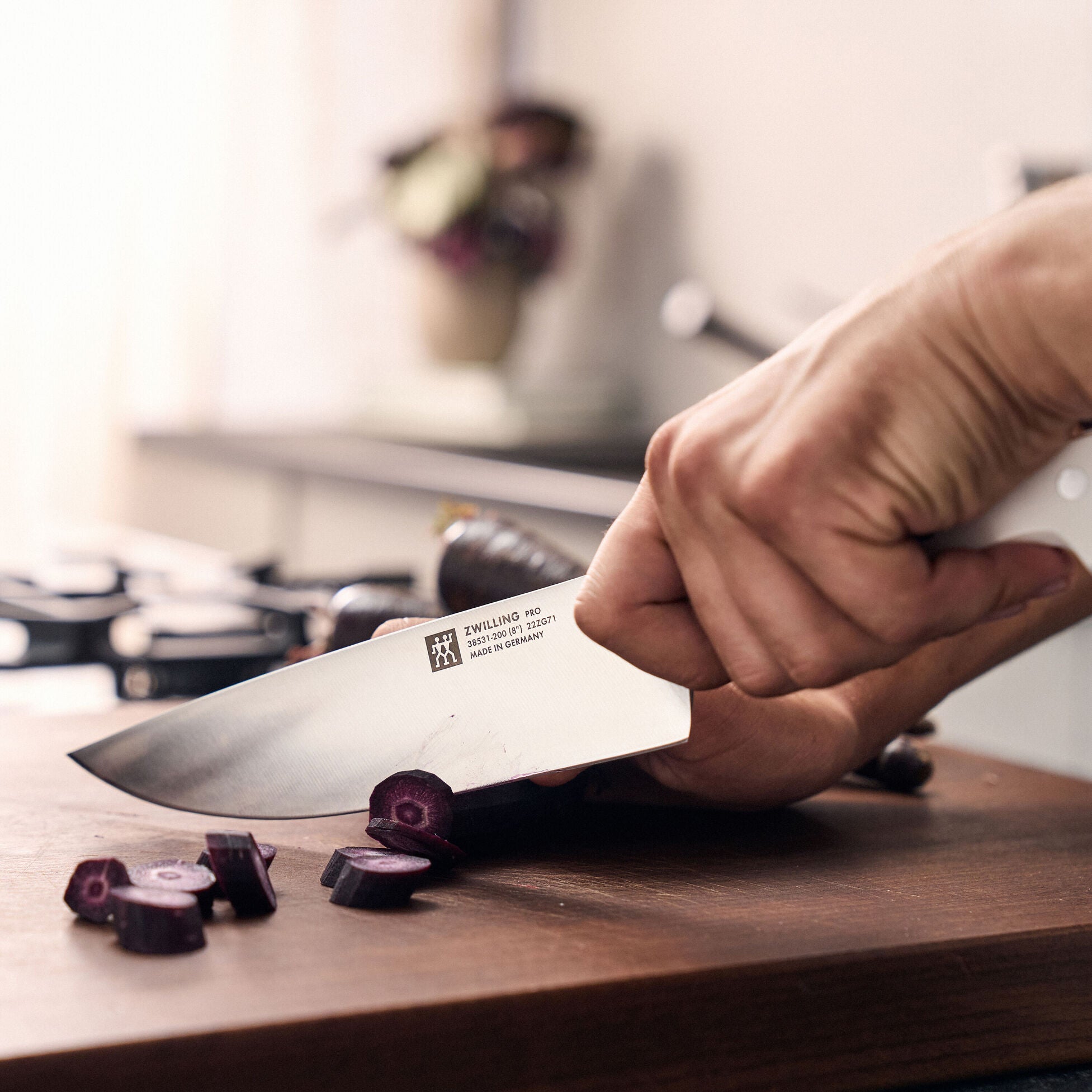 Person using a chef's knife to chop onions on a wooden cutting board with a blurred kitchen background.