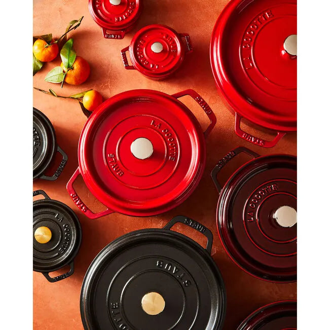 Collection of red and black cast iron cookware on a warm-toned surface with fruits.