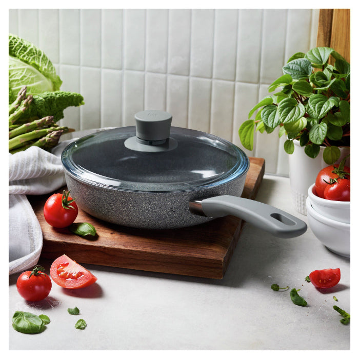 Gray cookware set on a kitchen counter with vegetables and plants.