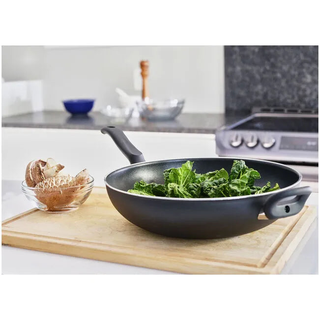 Black frying pan with greens on a wooden cutting board in a kitchen setting
