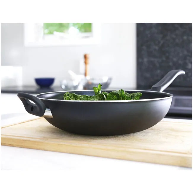 Black wok with green vegetables on a wooden cutting board in a kitchen setting