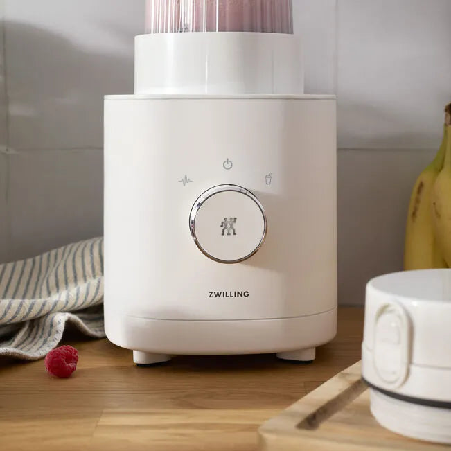 White blender with 'ZWILLING' branding on a kitchen counter with fruits and a mug.