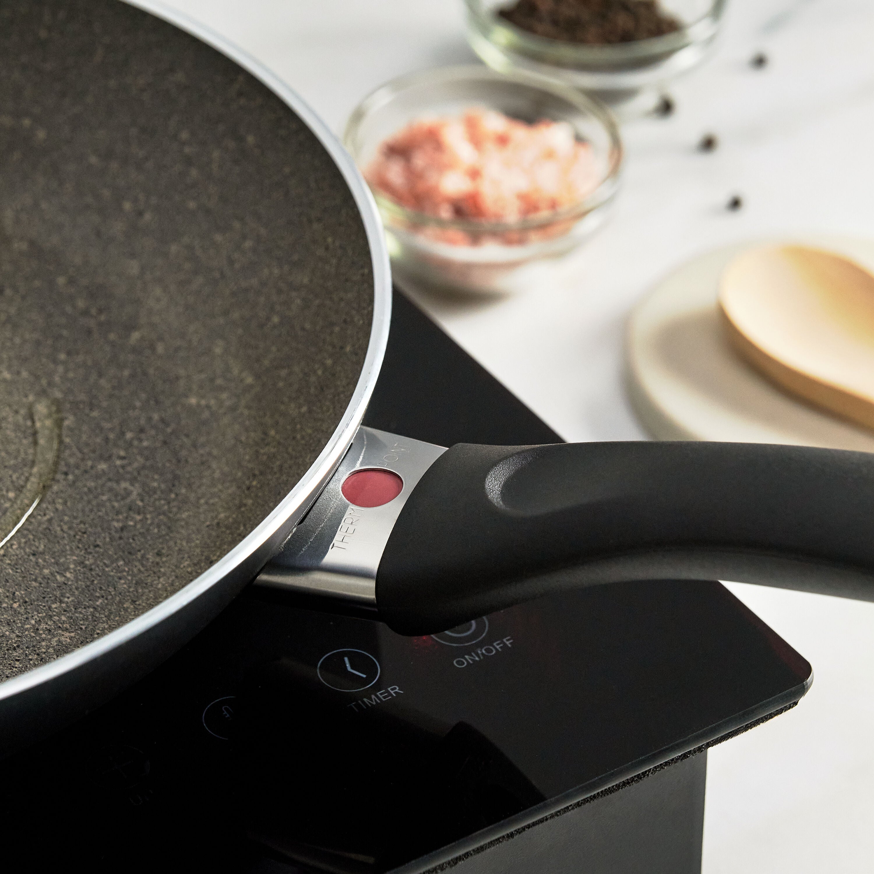 Frying pan on an induction cooktop with ingredients in the background