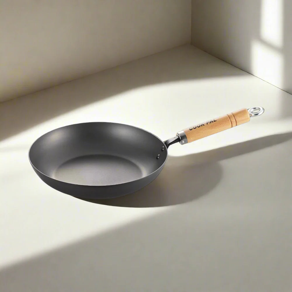 Black frying pan with a wooden handle on a light surface