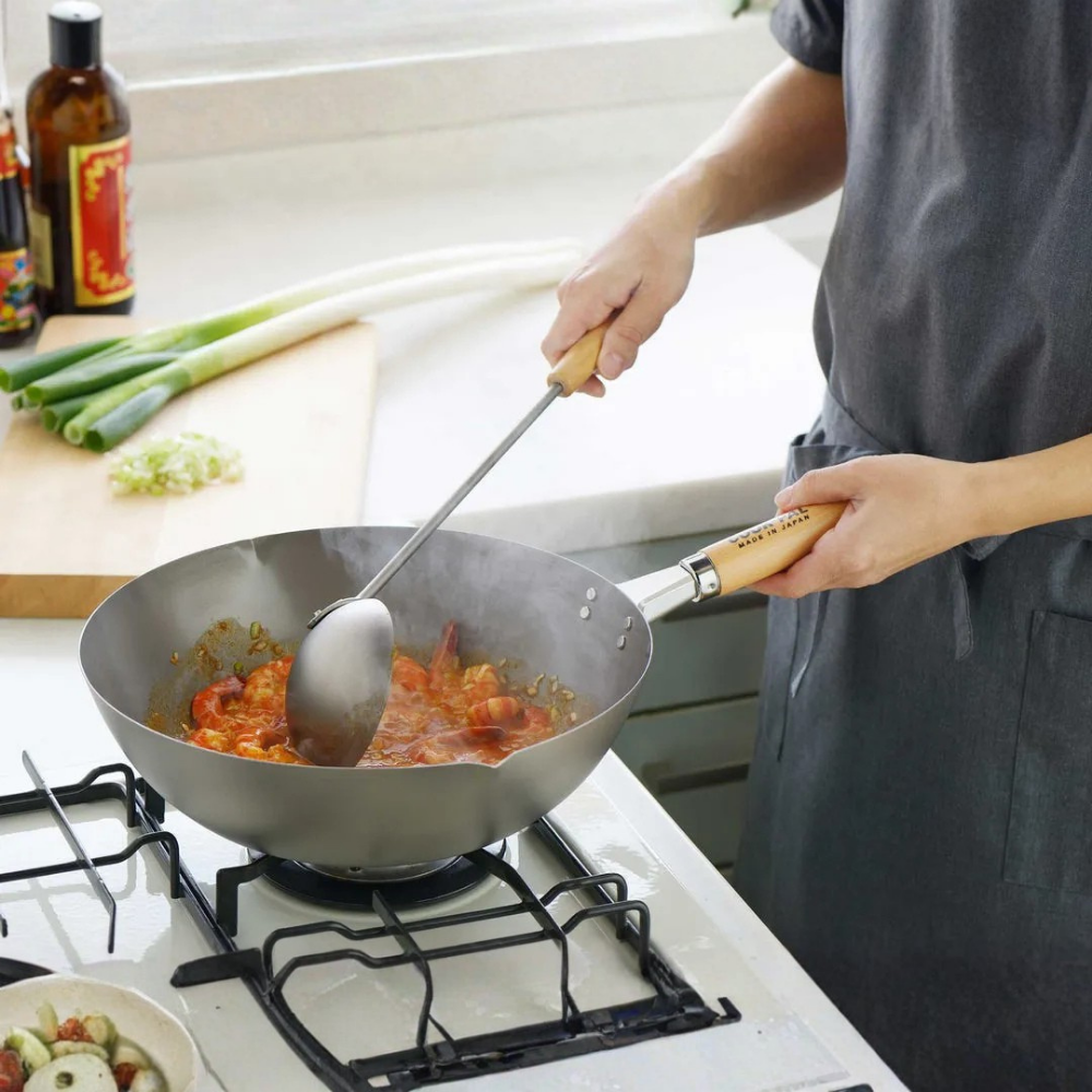 Person cooking in a kitchen with a wok and spatula on YOSHIKAWA COOK-PAL Titanium Wok 