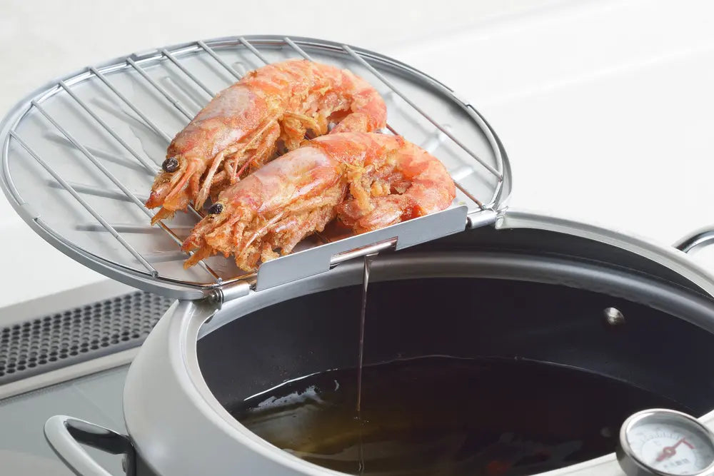 Shrimp being fried and dripping oil  with a thermometer attached.
