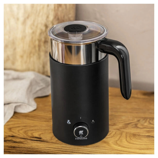 Black milk frother with stainless steel top on a wooden surface