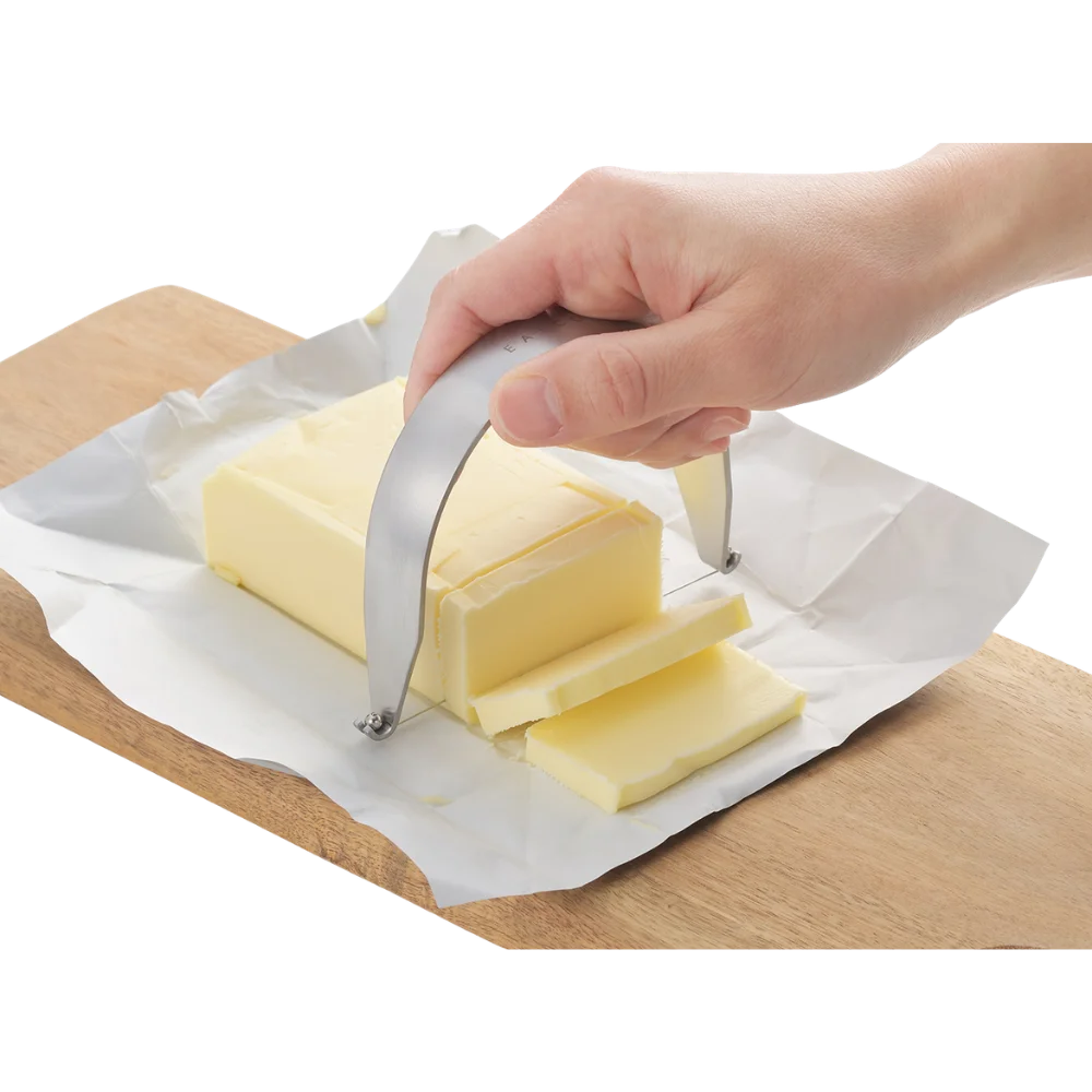 Hand using EAtoCO Kaku Wire Cheese Cutter for perfect slices on butter, showcasing precision and cleanliness. Stainless steel, made in Japan.